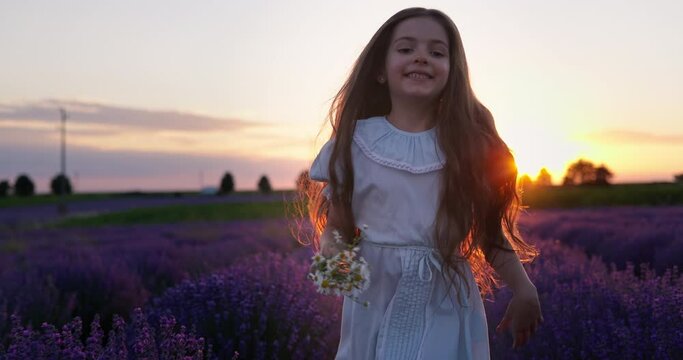 Happy carefree little girl with beautiful dress running in lavender field rows at sunset