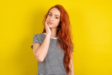 Photo of young beautiful red haired woman wearing striped shirt over yellow studio background enjoy fresh perfect smooth skin touch face