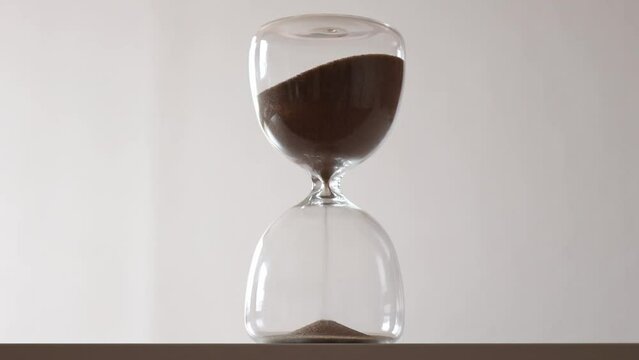 Sand goes through the bulbs of an hourglass on a white background