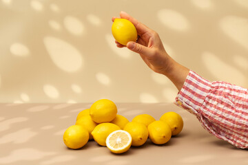 A woman takes a juicy lemon from the table on a beige background with shadows. Summer, exotic fruits.