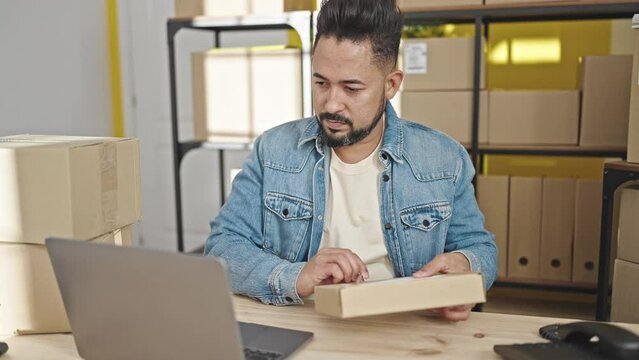 Young latin man ecommerce business worker using laptop writing on package at office