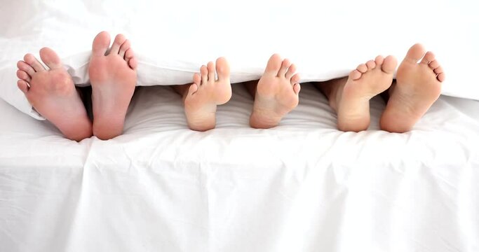 Legs of woman with two men in bed in bedroom. Polygamy in men and women