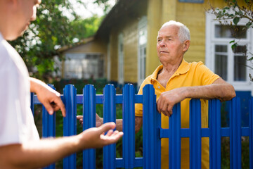 Neighbor conversation. Two smiling men breezily chatting near fence of rural house