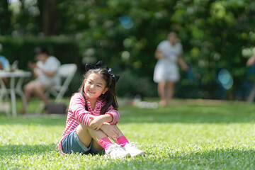 Naklejka na ściany i meble Adorable little Asian child girl sitting on the green lawn in the park.