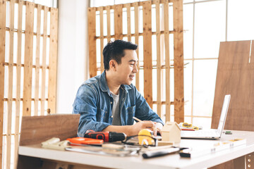 Middle age adult asian man carpenter using laptop for online working with customer wotk at home