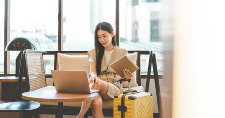 Business asian entrepreneur woman sitting in lounge with laptop and travel luggage © dodotone