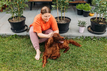 Cheerful happy young woman playing with her dog in the yard of the house in summer. Beautiful Irish...