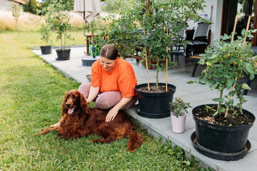 Cheerful happy young woman playing with her dog in the yard of the house in summer. Beautiful Irish...