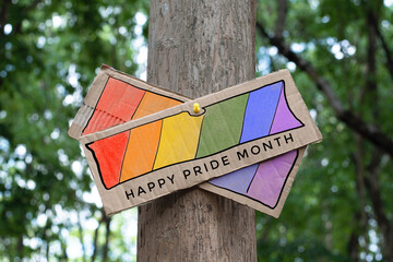 Signpost which has rainbow drawing with texts 'Happy Pride Month' sticked on tree trunk in public park to celebrate and to greet LGBT people events in pride month and to respect gender diversity.