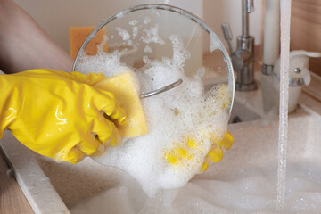 female hands in gloves wash dishes in the sink in the kitchen
