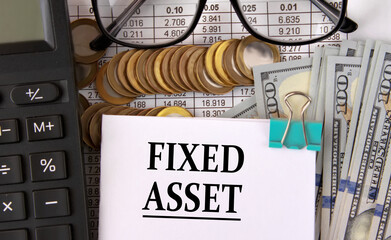 FIXED ASSET - words on a white piece of paper on the background of a calculator, pennies and glasses