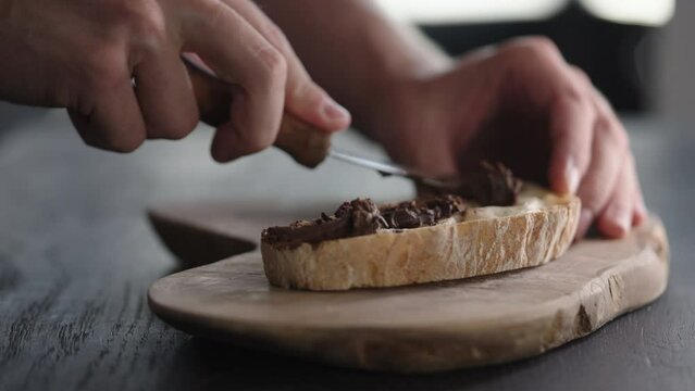 Slow motion man spreading chocolate hazelnut butter on ciabatta slice on olive board