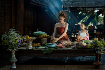 Pretty Asian girl wearing ancient native Northern Thai traditional dress costumes teaching her daughter to cook delicious food in the old style of Thai culture in the kitchen of a Thai house.