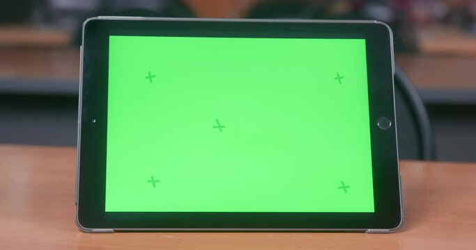 Digital tablet in a case is on the table, green chromakey with guide marks on the display, front view, close up. Gadget for work, online education or creativity. Template for advertising.