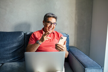 MIddle aged latin man using a smart phone on a couch at home