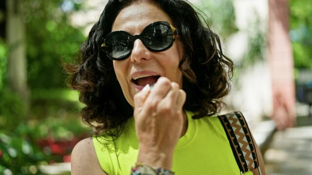 Middle age hispanic woman smiling confident applying lipstick at the street