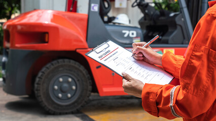 A mechanical engineer is using heavy equipment checklist form for inspecting the factory forklift vehicle (as blurred background). Industrial working with safety practice concept, selective focus.  - obrazy, fototapety, plakaty