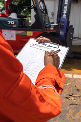 A mechanical engineer is using heavy equipment checklist form for inspecting the factory forklift vehicle (as blurred background). Industrial working with safety practice concept, selective focus.  © Nattawit