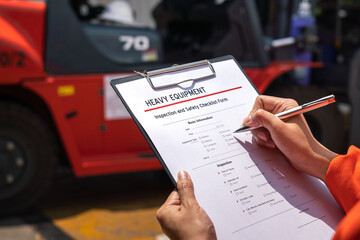 A mechanical engineer is using heavy equipment checklist form for inspecting the factory forklift vehicle (as blurred background). Industrial working with safety practice concept, selective focus. 