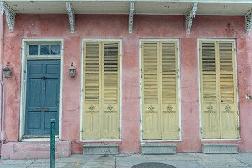 Beautiful home exterior in the French Quarter in New Orleans, Louisiana. Shallow focus for artistic effect on the fleur de lis on the left-most yellow shutter. - obrazy, fototapety, plakaty