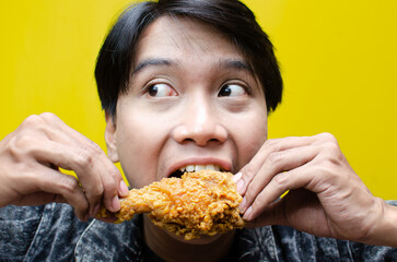 Funny expressive asian man holds fried chicken with wow expression isolated over yellow background....
