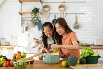 Portrait of enjoy happy love asian family mother with little girl daughter child help cooking food healthy eat with vegetable testing smell soup in pot with spoon.helping mommy in kitchen at home