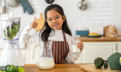 Obraz na płótnie Canvas Portrait of enjoy happy little asian child girl smiling having protein breakfast drinking and hold glasses of fresh milk,healthy nutrition,calcium and vitamin,dairy product,strong, growth in kitchen