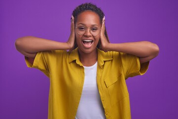 Young expressive ethnic African American woman covers ears with hands and screams loudly not...