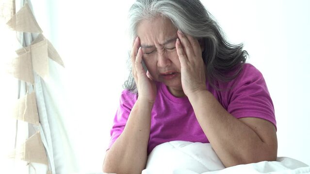 Asian elderly woman sitting on the white bed Having a headache Because it is a disease related to pressure and migraine, to retirement age and health care concept.