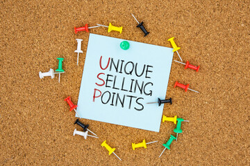 Unique selling points text on light blue post-it paper pinned on bulletin cork board surrounding by multi color pins. This message can be used in business concept about unique selling points.