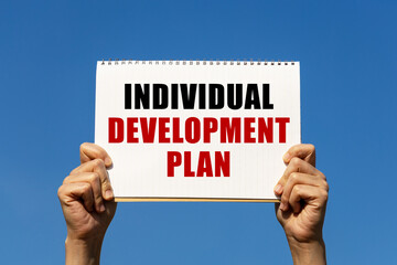 Individual development plan text on notebook paper held by 2 hands with isolated blue sky background. This message can be used as business concept about individual development plan.