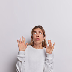 Young European scared with her arms up like something falling from above holds breath from amazement dressed in casual jumper isolated over white background blank space for your promotional content