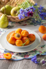 Summer mood: fresh apricots, pears and cornflower flowers on a wooden background surrounded by vintage crockery. Close up