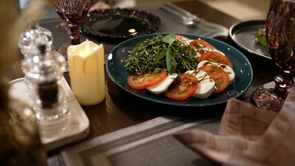 A plate of tomatoes and cheese is served on the table. The waiter serves a dish of tomatoes and cheese. The hands of the waiter put a plate of salad on the table. 