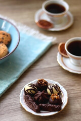 Plate of chocolate pralines, bowl of cookies, cups of tea, glasses of juice and lit candles on the table. Selective focus.