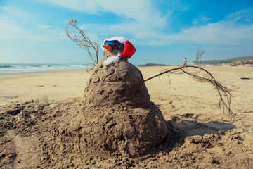 Funny Snowman in Sunglasses and Santa Red Hat, made of the Sand on Goa beach, India - obrazy, fototapety, plakaty