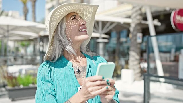 Middle age grey-haired woman tourist smiling confident using smartphone at coffee shop terrace