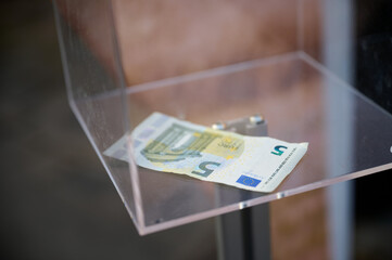 Ein einzelner Fünf-Euro Schein liegt in einem durchsichtigen quadratischen Spenden-Sammelbehälter...