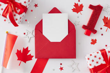 Canada Day celebration theme. Top view flat lay of open red envelope with blank card, gift boxes, canadian flag, red maple leaves, stars on white background with empty space for text