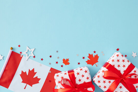 Gifts for celebrating Victoria Day concept. Top view flat lay of patriotic gift boxes, canadian flag, maple leaves, event confetti on light blue background with empty space for text or promo
