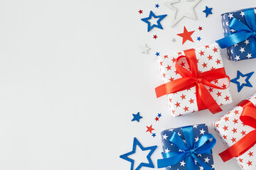 Fototapeta na wymiar Idea of American Independence Day gifts. Top view flat lay of gift boxes in national colors, festive confetti on white background with empty space for message or advert