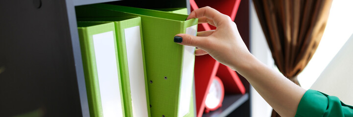 Woman taking off green folder with documents from shelf