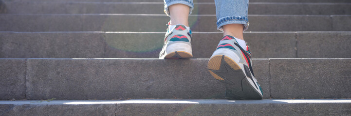 Woman legs in jeans and sneakers going up steep stairs