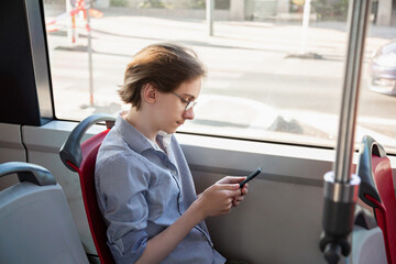 Tennager boy in a tram holding mobile phone in his hand. Guy siting near a window, looks with interest at screen of smartphone, playing mobile games online on smartphone connected to public wifi