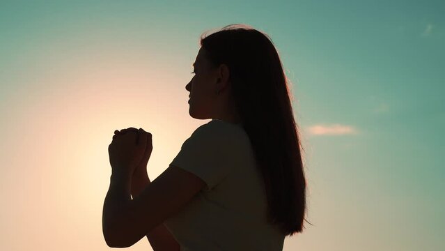 Young woman praying at sunset, Silhouette. Path of soul to God through prayer. Christian prayer, nature. Morning prayer of girl outdoors. Freedom of religion. Era of mercy, kindness, love. Girl, relax