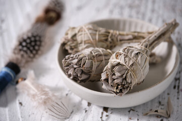 White Sage smudge sticks (Salvia apiana) in a white bowl with smudging feather on old white wooden table