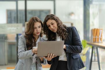 Young businesswoman and accountant talking with laptop and tablet Two attractive millennial Caucasian businesswomen are planning their projects together.