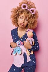 Pregnant woman cradles collection of baby item has sad tired expression dressed in pajama prepares for new chapter of motherhood looks unhappily isolated over pink background. Hopes of growing family.