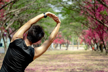 Asian athlete man with well trained body in black sportswear stretching arms and shoulders overhead. Cool down after outdoor exercise in the park. Physical exercise posture for muscle stretching.