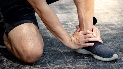 Asian athlete man touching foot in pain due to sprained ankle while running in the park. Broken...